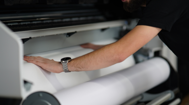 Ein Mitarbeiter wechselt an einer Druckmaschine die Papierrollen aus.